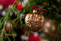 Gold Heart Ornament on the Branch of a Christmas Tree with Lights and Tree in the Background