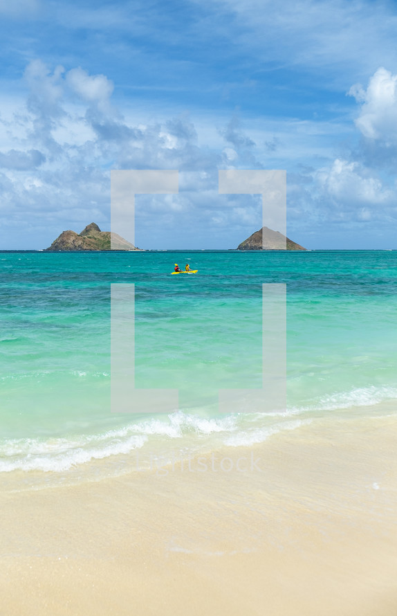 White sand beach on Hawaii coast with kayakers and islands on the horizon
