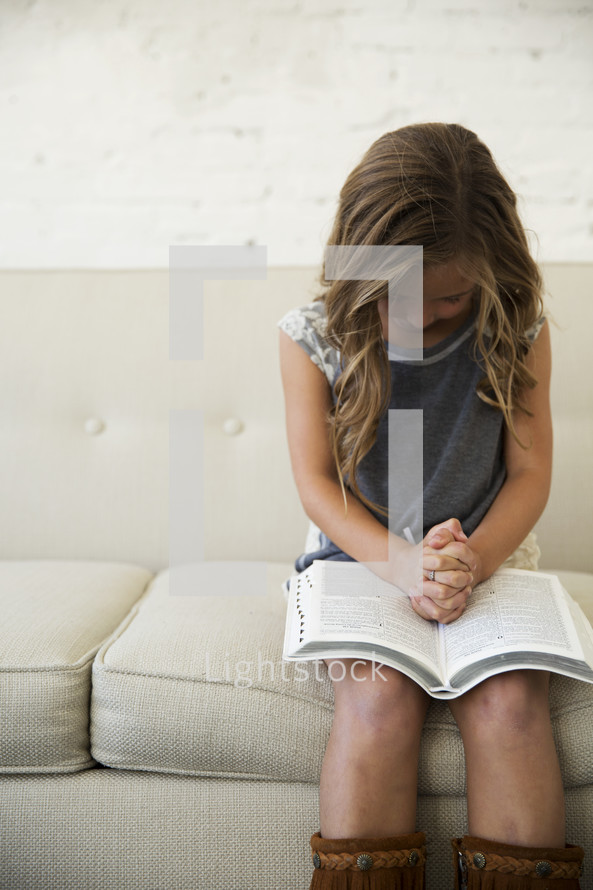 girl child with praying hands over the pages of a Bible 