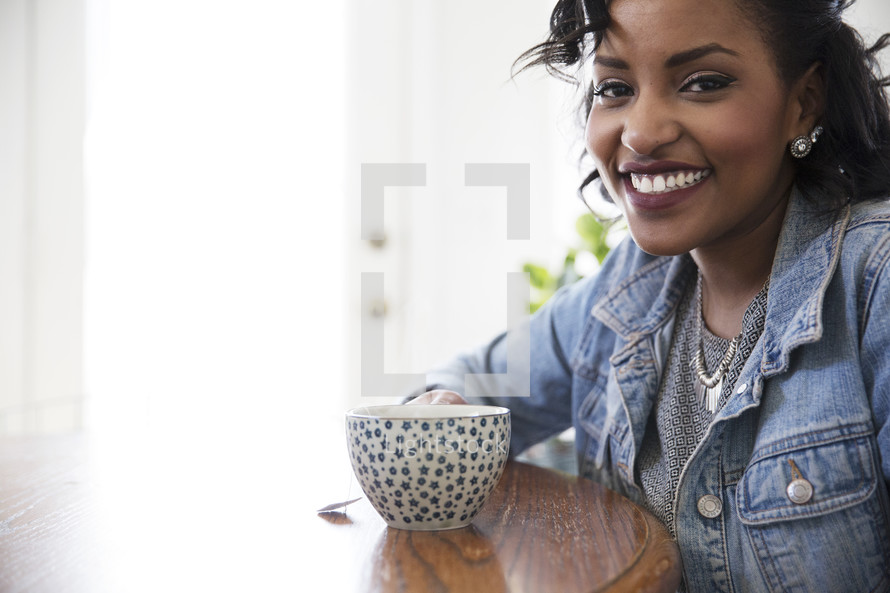 an African American woman sitting at a table with a coffee cup 