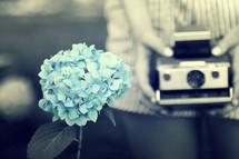 Hands with Polaroid camera and blue flower.
