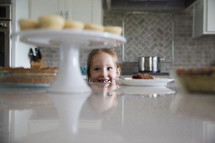 a little girl looking up at dessert on the counter in the kitchen 