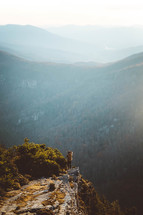 a person standing at the edge of a mountain cliff taking in a mountain view 
