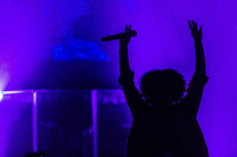 A woman on stage with her arms raised in worship.