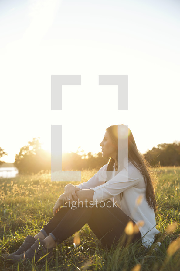 a woman sitting in the grass under sunlight 
