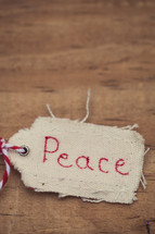 A fabric Christmas gift tag, labeled "Peace," on a wood grain background.