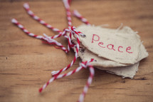 A stack of Christmas gift tags, the top one reading "Peace," on a wood grain background.