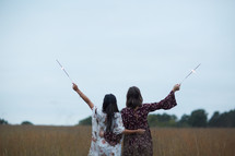 young women holding sparklers in a field  
