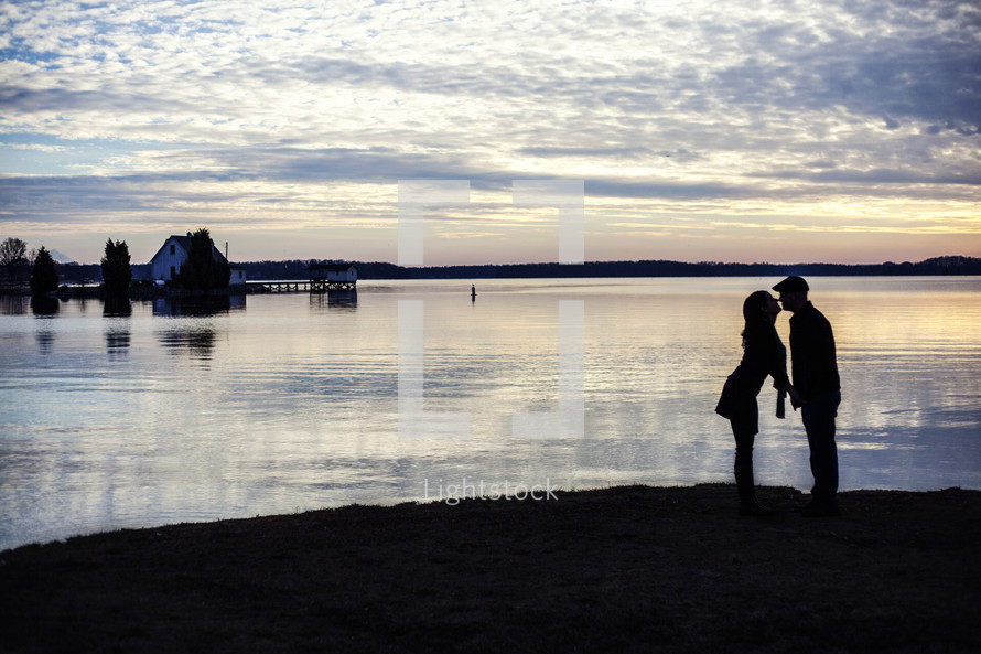 silhouette of a couple kissing in front of water