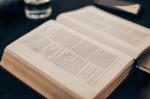 open Bible on a table with a glass of water and journal 