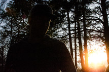 a man standing in a dark forest at sunrise 