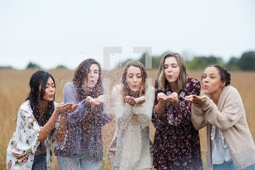 group of young women blowing confetti standing in a field 