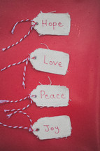 Christmas gift tags reading "Hope," "Love," "Peace," and "Joy" on a red background.