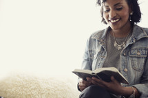 An African American woman sitting in a chair reading a Bible 