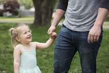 A little girl holding hands and laughing with her father.
