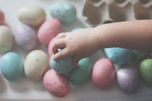 a toddler touching dyed speckled Easter eggs 