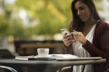 a woman checking her cell phone at an outdoor coffee shop.