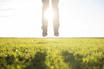 person jumping in green grass at sunrise. 