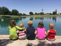 kids sitting by the edge of a pond 