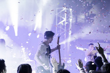 Silhouette of audience during a concert performance on stage with confettii in the air.