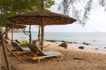 lounge chairs under a straw umbrella on a beach 