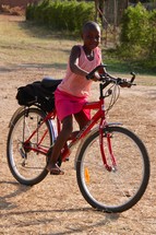 a girl riding a bicycle on a dirt road 