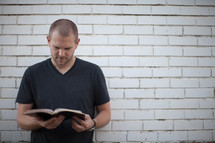 a man reading a Bible standing in front of a white wall 