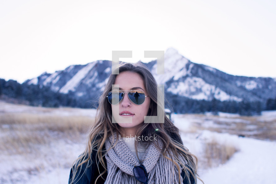 A young woman in sunglasses standing in front of a snow capped mountain 