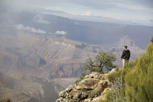 man standing on a mountainside cliff looking out at canyons 