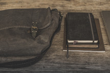Notebooks and a Bible on a table next to a blue bag