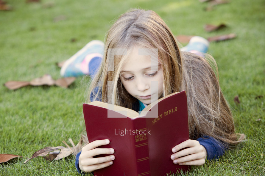 Little girl reading the Bible outdoors