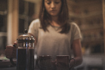 A woman pouring coffee into mugs from a french press
