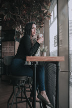 a young woman with a coffee cup sitting in a window seat at a coffee shop 