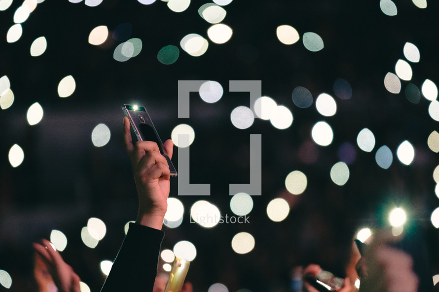 cellphones taking pictures of bokeh lights at a concert 
