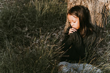 a little girl praying under a tree 