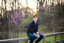 a young man sitting on a wood railing outdoors 
