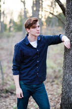 a young man leaning against a tree 