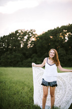 a teen girl with a lace blanket standing in the grass