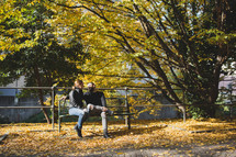 a couple sitting on a park bench in fall 