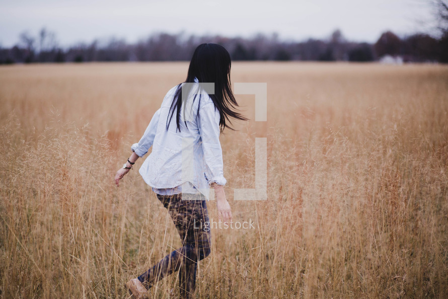 a woman walking through a field of tall grass 