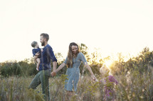 a family walking through a field of tall grasses holding hands 