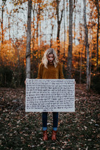 portrait of a woman standing outdoors holding a Bible verse sign 