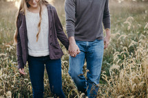a young couple holding hands walking through a field of tall grass 