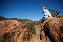 a woman sitting on a red rock with mountain view 