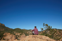a man sitting on a rock looking out at mountains 