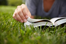 a person sitting in the grass reading a Bible.