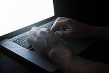 a man's hands typing on a laptop in darkness 