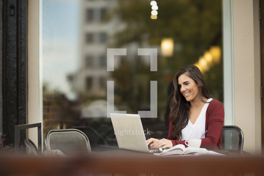 a young woman sitting at a table outdoors working at a laptop computer 
