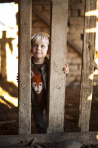 A toddler boy looking through the pickets of a fence.