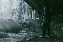 a man standing in a cave watching a waterfall 